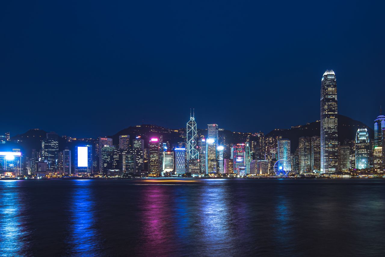 contact-img Stunning night view of Hong Kong's illuminated skyline reflecting on water, showcasing vibrant city lights.