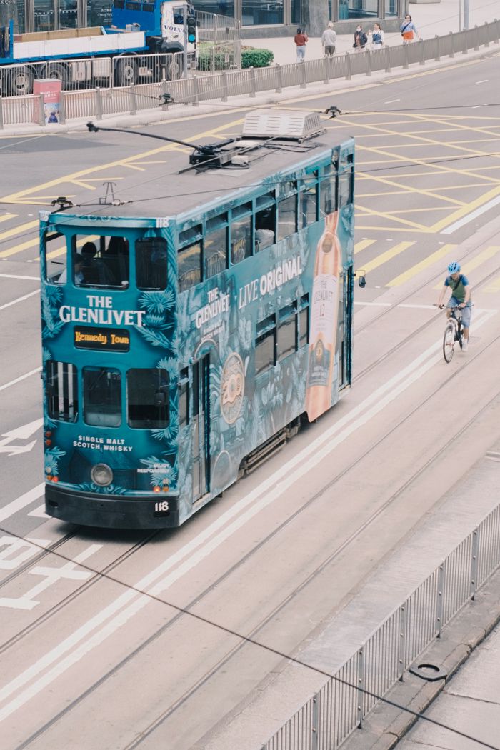 why-choose-us Double-decker tram with vibrant advertisement on Hong Kong streets showcasing public transportation.