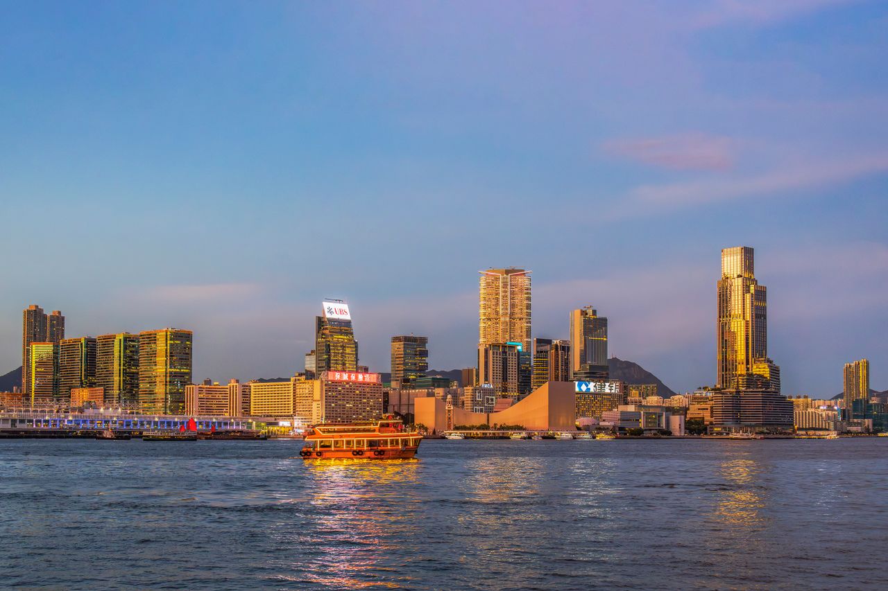services-03 Dramatic view of Hong Kong's skyline and ferry on Victoria Harbour at sunset.