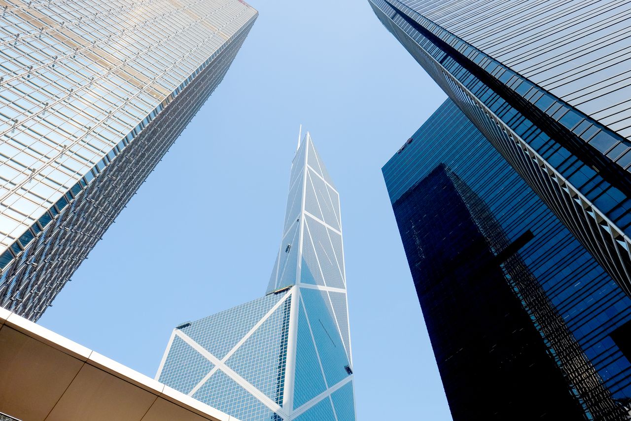 gallery-5 Dynamic upward view of iconic Hong Kong skyscrapers against clear blue sky.